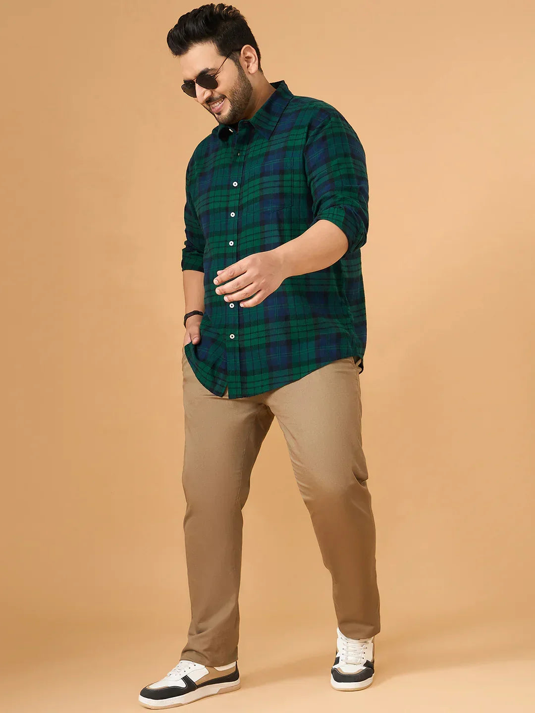 Plus size man in green checked shirt, khaki pants, and sneakers on beige background