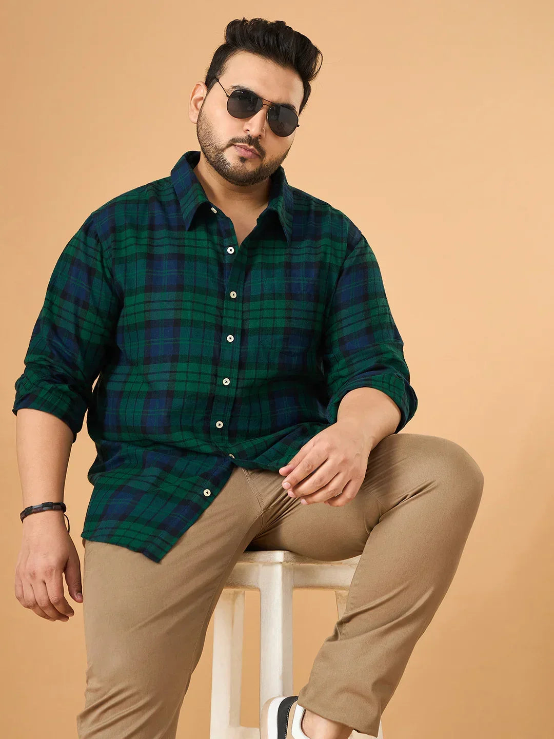 Plus size man in green checkered shirt, khaki pants, and sunglasses sitting on a stool