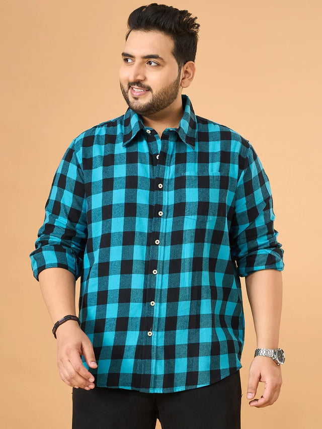Plus size man in blue and black checked casual shirt with rolled sleeves against beige background