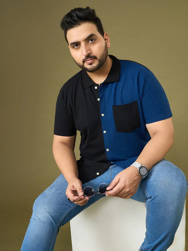 Plus size man in a two-tone black and blue short sleeve shirt and jeans holding sunglasses