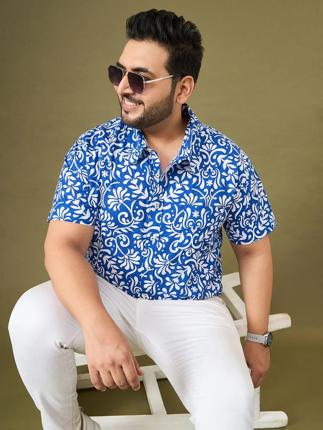 Plus size man in blue floral print shirt and white pants, wearing sunglasses, seated