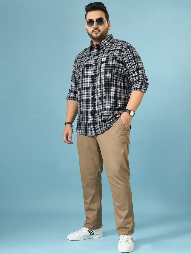 Plus size man wearing black checked shirt and beige pants with sneakers, standing on blue background