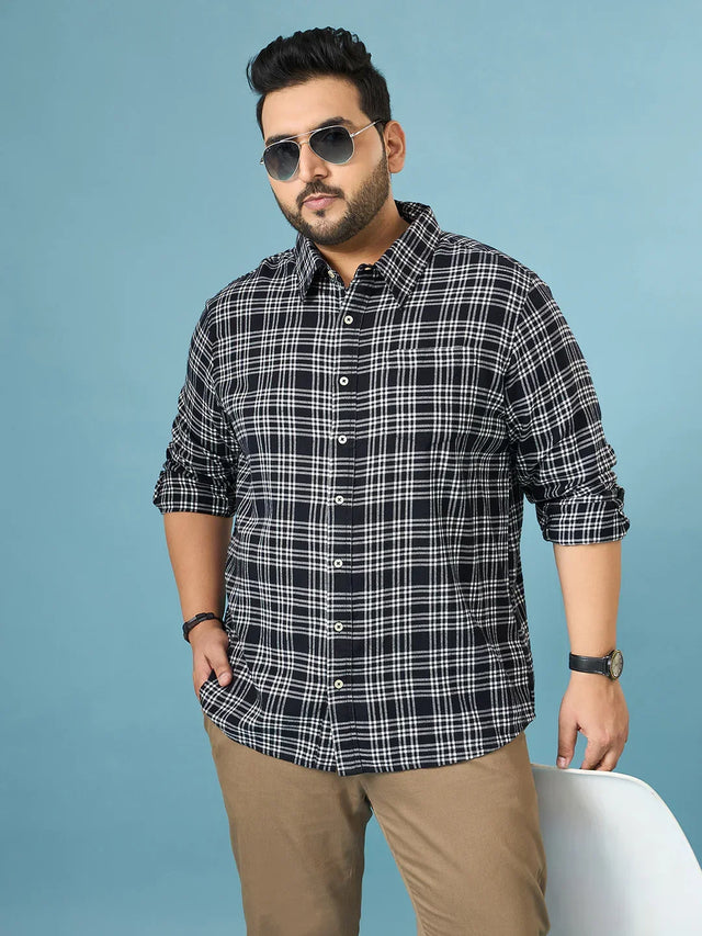 Plus size man in black and white checkered shirt and beige pants, posing confidently
