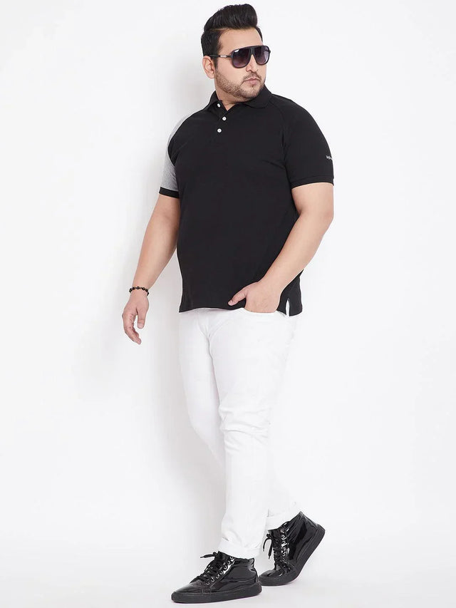 Plus size man in black polo t-shirt, white jeans, black sneakers, and sunglasses posing