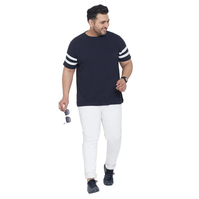 Plus size man wearing navy t-shirt with white sleeve stripes and white jeans