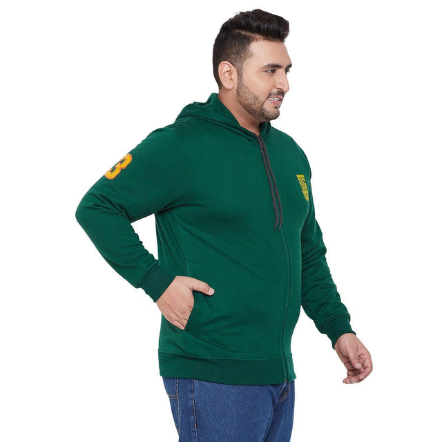 Plus size man wearing green zip-up hoodie with yellow patch and blue jeans, side view