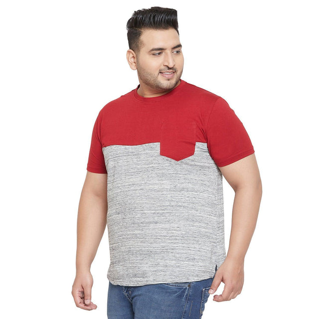 Plus size man wearing a red and grey colorblock t-shirt and blue jeans, posing against white background