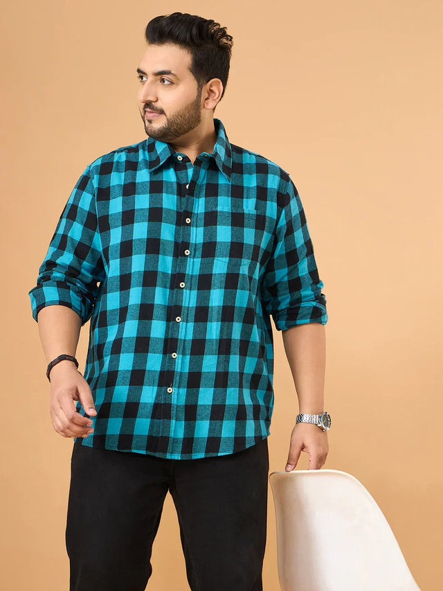 Plus size man in blue and black checkered shirt and black jeans standing indoors