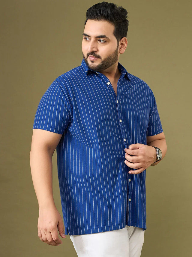 Plus size man in blue striped short sleeve shirt and white pants, posing against tan background