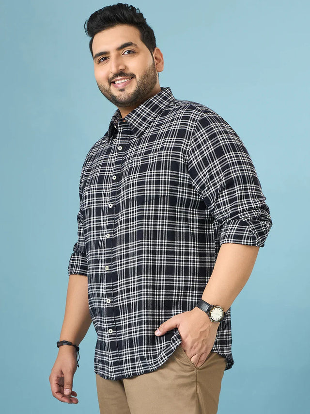 Plus size man in black and white plaid shirt and khaki pants smiling against blue background