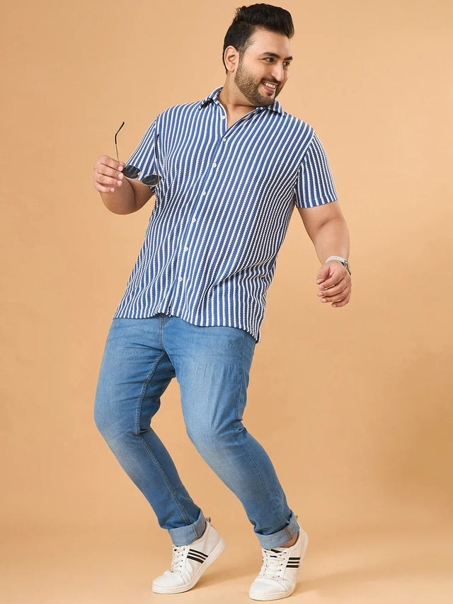 Plus size man wearing blue striped shirt and light blue jeans, posing with sunglasses