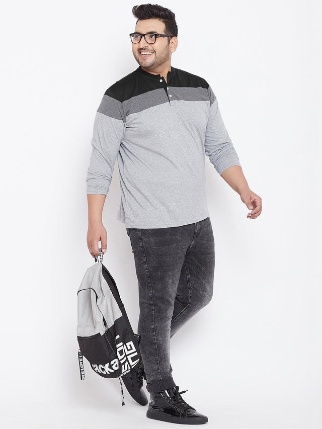 Plus size man in grey and black colorblock henley t-shirt, black jeans, sneakers, holding a backpack