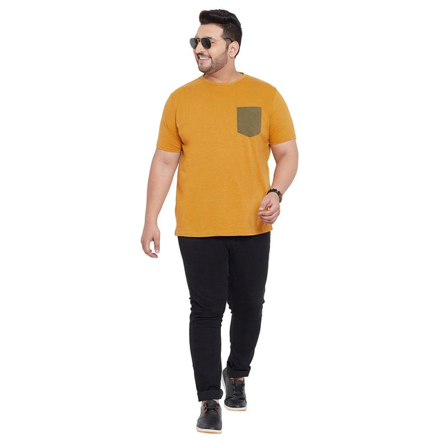 Plus size man wearing mustard t-shirt with olive pocket and black jeans, walking confidently