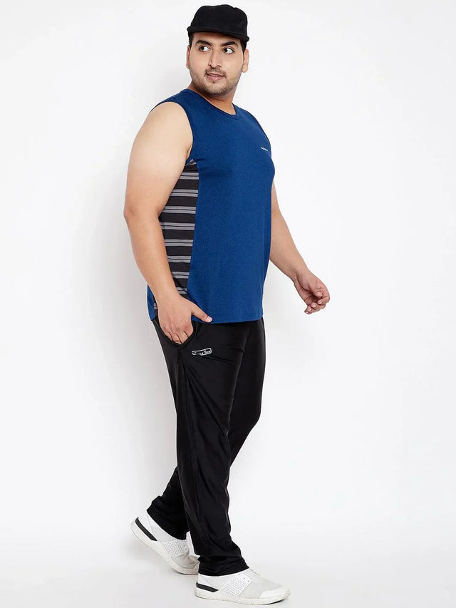 Plus size man in blue sleeveless t-shirt, black joggers, and cap, posing against white background