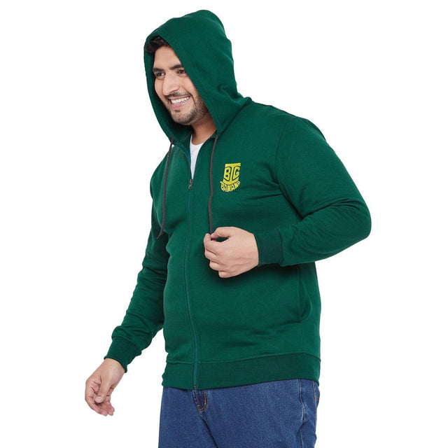 Plus size man in a green zip-up hoodie with hood, yellow chest logo, and blue jeans